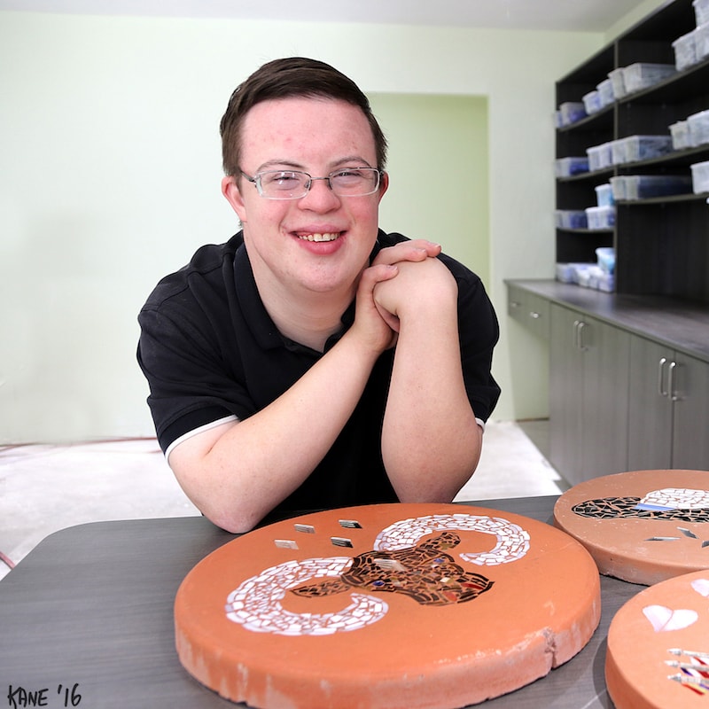 Man smiling in front of hand-made mosaic artwork