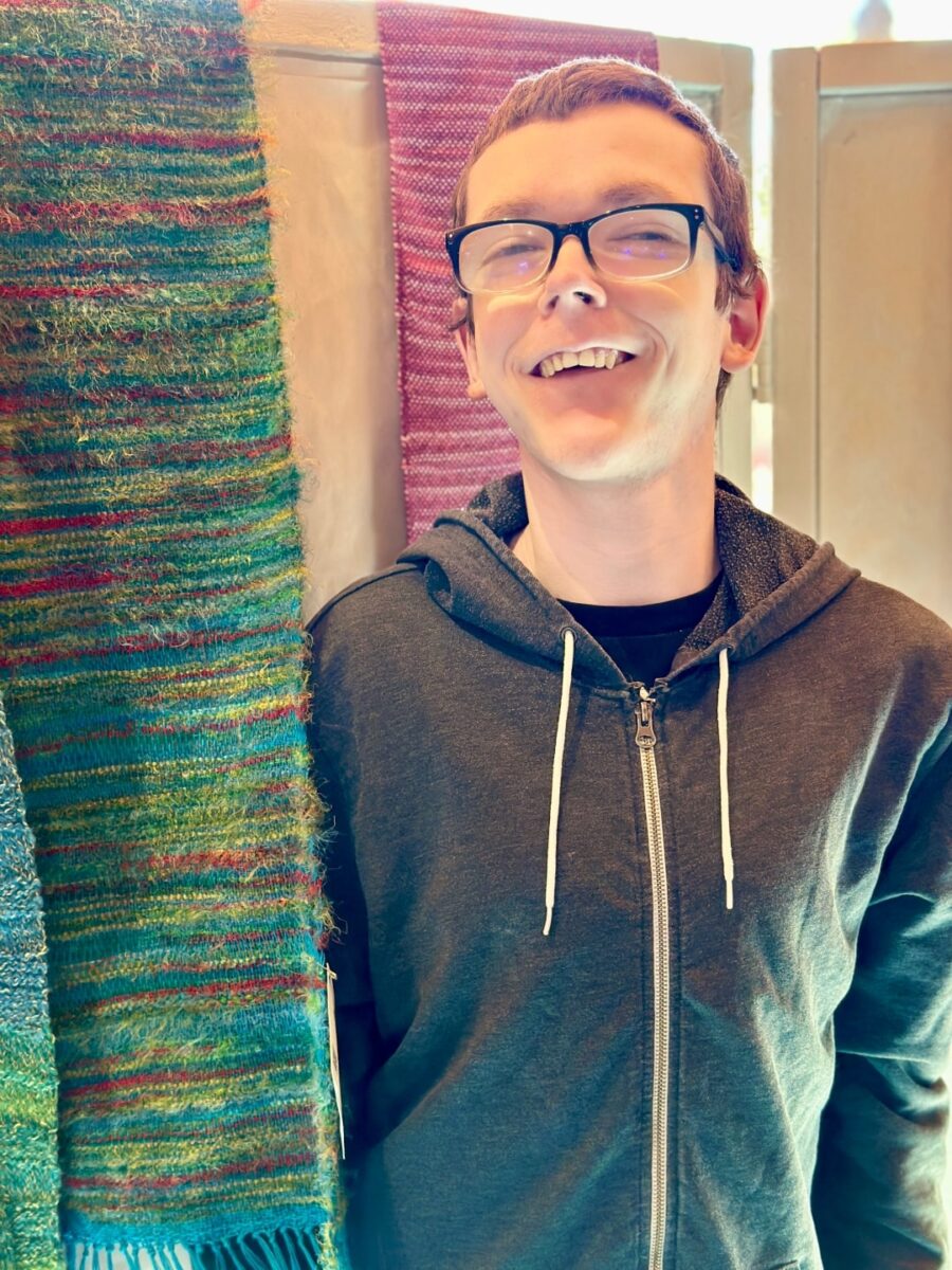 In the weaving studio at Rainbow Acres, an adult with developmental disabilities is engaged in weaving a patterned textile.